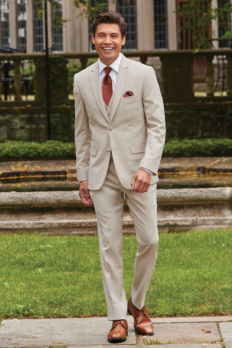 man in courtyard wearing the tan stretch suit with a burnt orange tie and pocket square