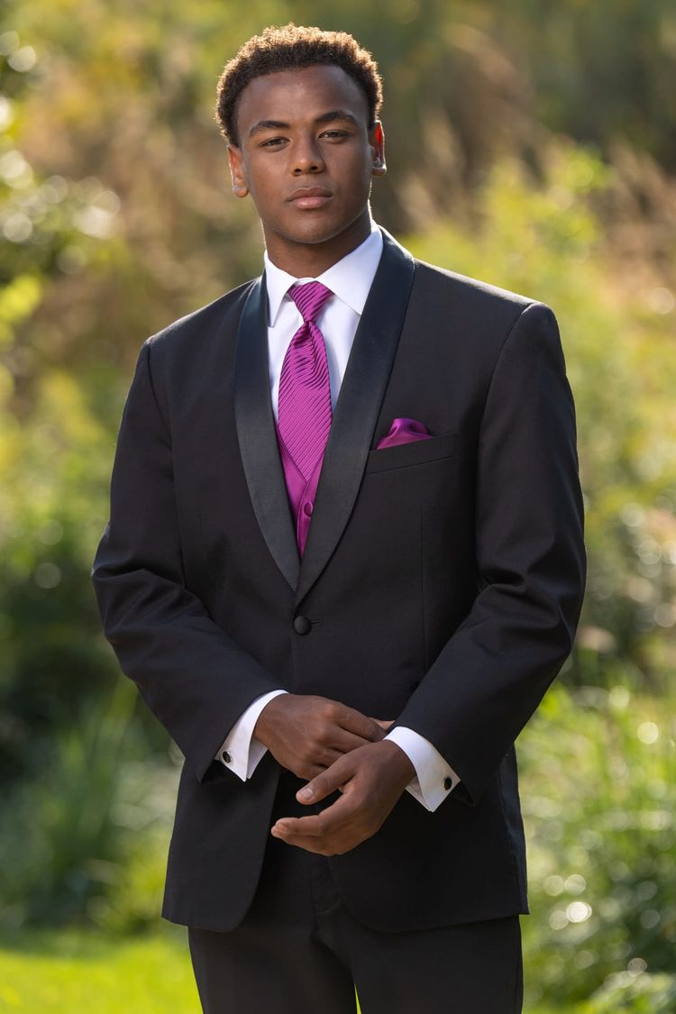 A prom guy wearing the Black Cyprus Tuxedo, white shirt, and begonia colored vest and tie